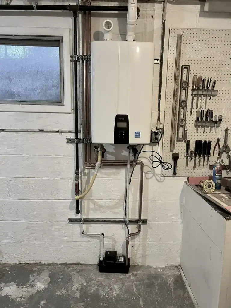 Wall-mounted boiler with exposed plumbing in a basement utility room next to a pegboard of tools.