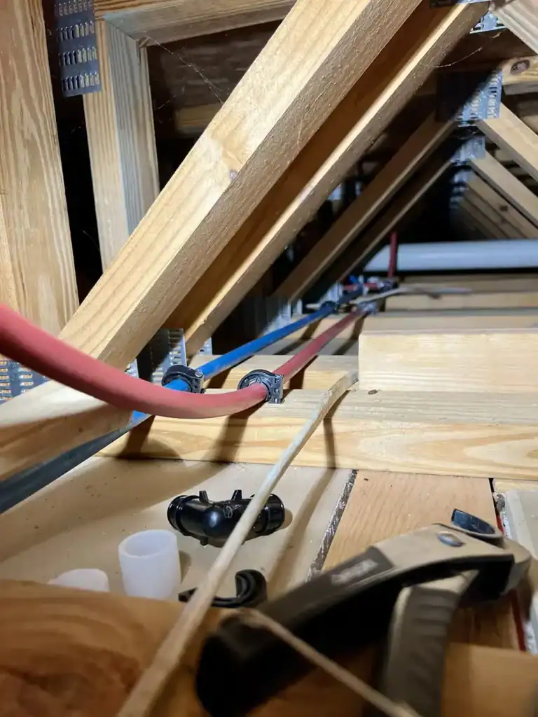 Attic space with exposed wooden framing and tangled red and blue electrical cables.