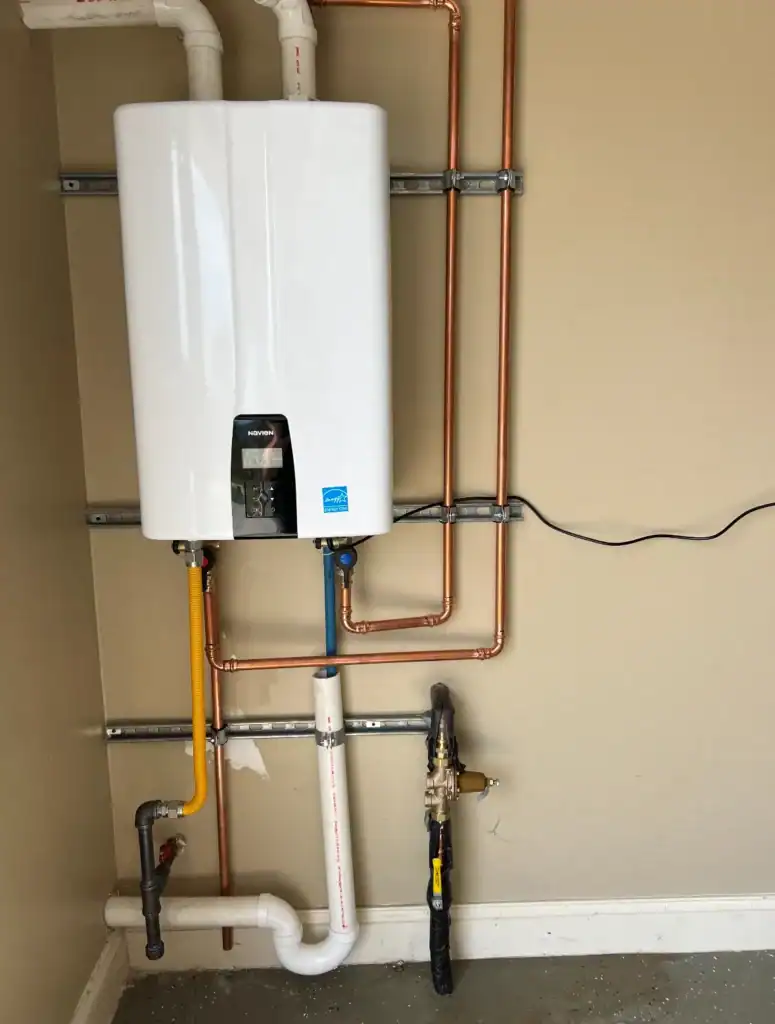 White wall-mounted boiler with copper and PVC pipes, valves, and a drain line in a utility room.